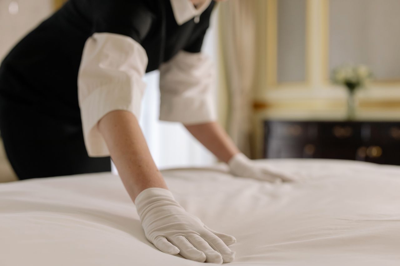 A housekeeper is smoothing the bed linens in a refined hotel room.
